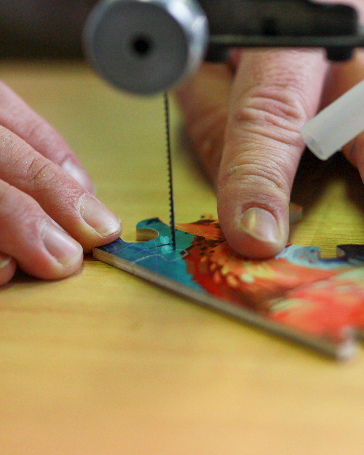 Deux mains façonnent un puzzle en bois à la scie à chantourner, gros plan sur la découpe en action